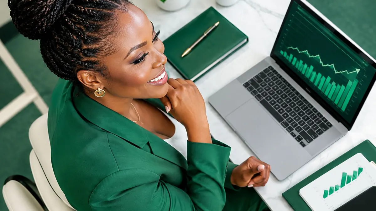 Seorang perempuan tersenyum sambil membaca grafik naik di laptop, dengan catatan di meja